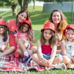 Friends enjoying a sunny day picnic on grass with bucket hats and smiles in a Portuguese park.