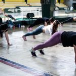 Group of women doing push-ups in a gym reflecting in a mirror.